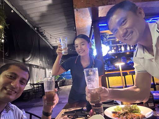 A group of people is gathered at a bar or restaurant in Thao Dien, Saigon, raising their glasses for a toast.