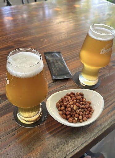 A wooden table set for a casual drink and snack session featuring two glasses of beer with foam heads, one on the left side partially filled to just b