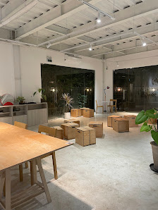 The image depicts an interior space that appears to be a modern office or co-working area with large windows allowing natural light in, and various wo