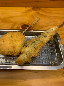 The image shows a close-up of two pieces of fried food on a metal tray with a wooden stick in one piece, likely tempura or similar battered and deep-f