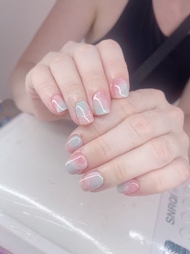 A close-up of a person's hands displaying their manicured nails painted in pink and grey gradient colors.