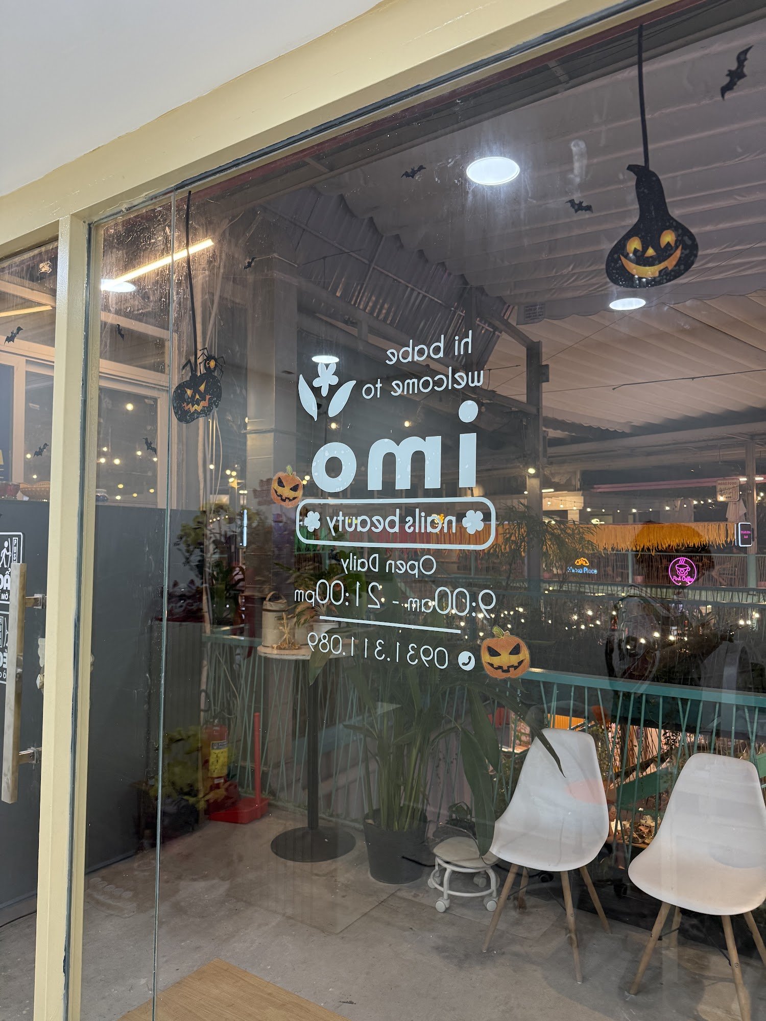 Exterior view of a nail beauty salon named 'omi nails beauty' in Thao Dien, Saigon. Features glass doors/windows with Halloween-themed decorations (pu