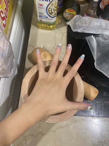 A close-up of a person's hand resting on a wooden mortar and pestle placed on a kitchen counter with various cooking ingredients in the background.