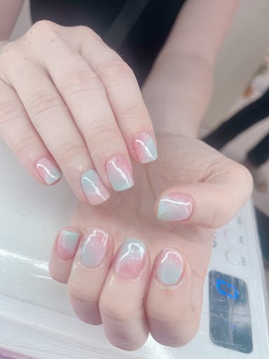 A close-up of a person's nails showcasing a pastel ombre nail polish design with a glossy finish.