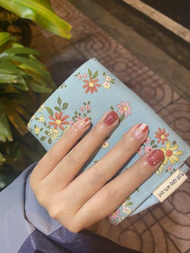 A close-up of a hand holding a floral-patterned wallet against an indoor background with green plants and patterned flooring, suggesting the photo was