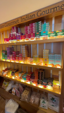 A shelf in a store displaying various packaged food items labeled 'Gourmet Indian Gourmet'. The products are neatly organized on three shelves, with t