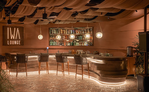 The image depicts the interior of IWA Lounge, a venue in Thao Dien, Saigon. It features a curved bar with integrated lighting, several high-backed cha