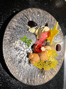 A plated dish featuring a variety of ingredients including what appears to be truffle slices, a red sauce or puree, and garnishes such as microgreens 