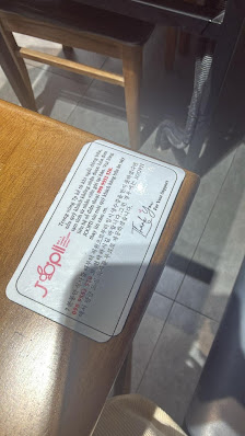 A close-up of a menu placemat on a wooden table in an indoor setting with natural light coming through the window.