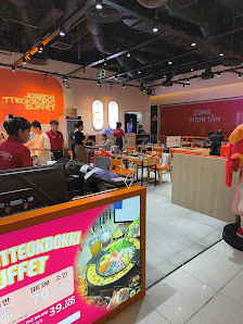 The image depicts the interior of a venue in Thao Dien, Saigon. It features a bright, modern space with white tiled flooring, orange and red signage, 