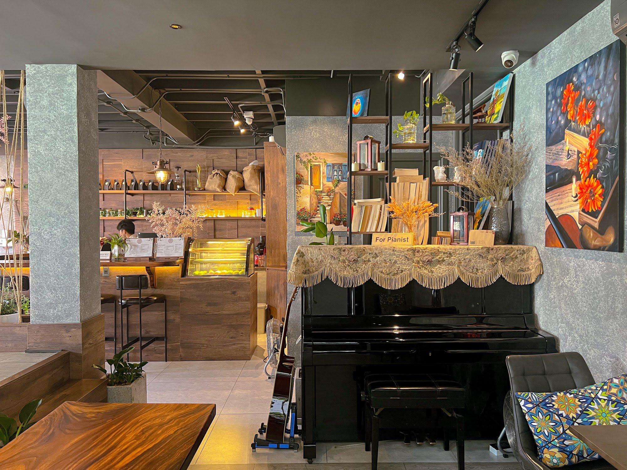 The image shows an interior view of a cozy café or restaurant in Thao Dien, Saigon. The space is well-lit with warm lighting and features wooden furni