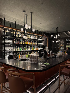 The image depicts a modern bar interior featuring a sleek black countertop and shelves stocked with various bottles of alcohol. The lighting is warm,
