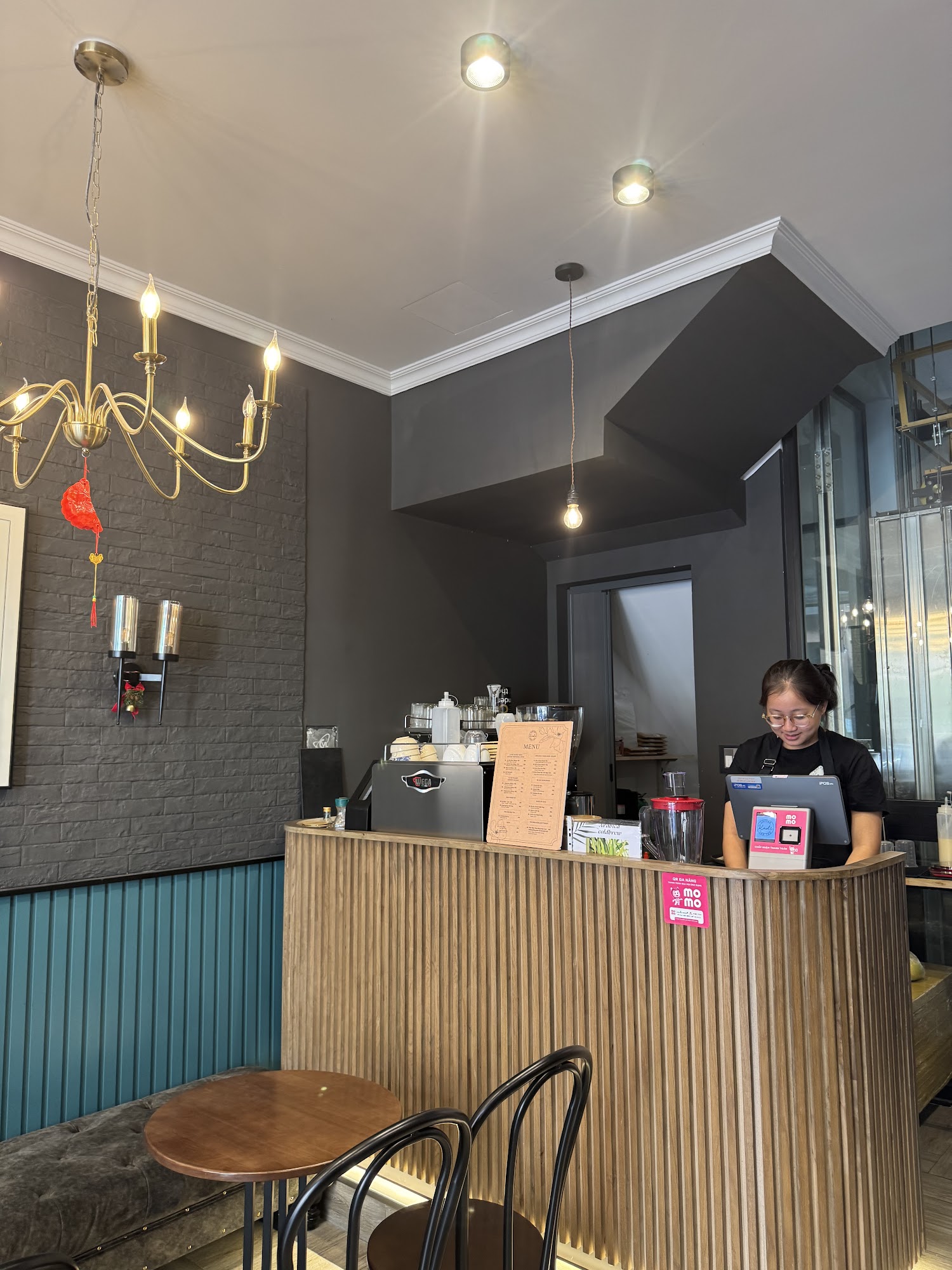 The image shows an interior view of a modern coffee shop or cafe in Thao Dien, Saigon. The decor includes dark brick walls and wooden paneling with me