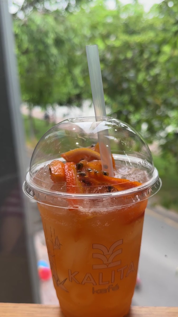 A close-up of a beverage in an orange plastic cup from 'Kalita' brand with visible ice cubes and pieces of fruit, possibly mango or papaya, floating o
