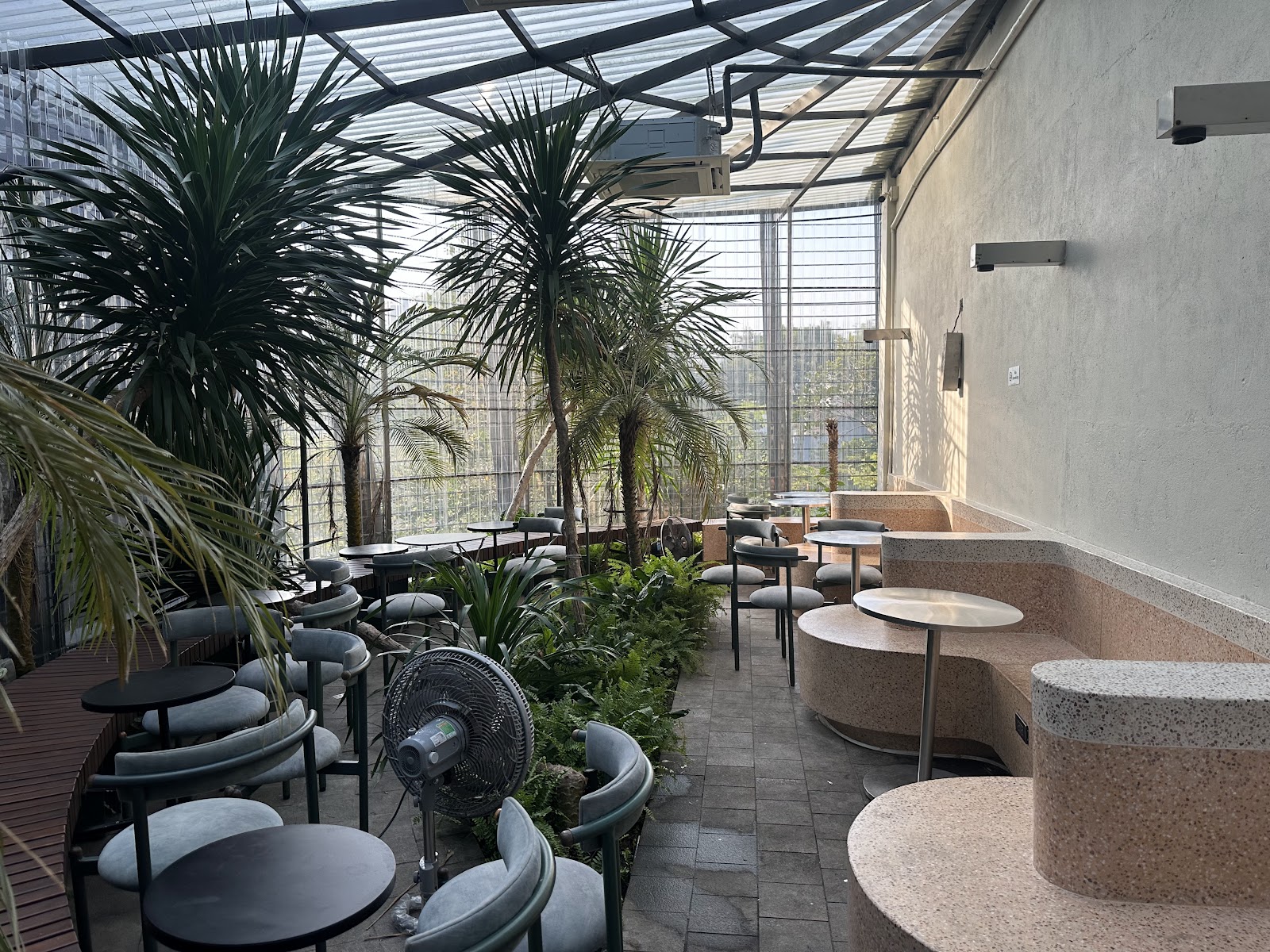 The image shows an indoor seating area of a venue in Thao Dien, Saigon. It features modern decor with various types of plants and trees providing gree