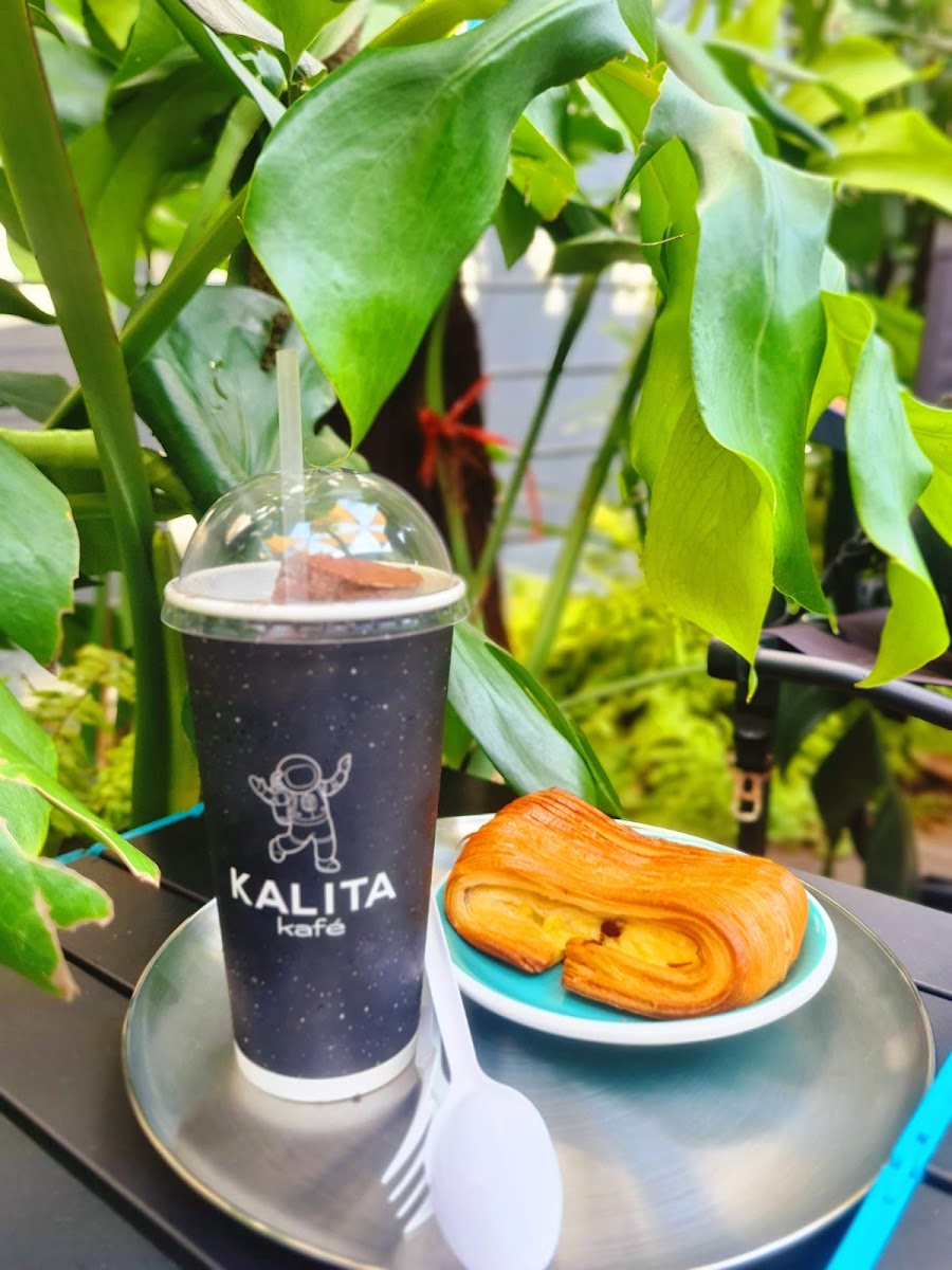 A beverage and pastry are displayed on a table amidst lush green foliage in what appears to be an outdoor setting of Kalita Café, Thao Dien, Saigon.