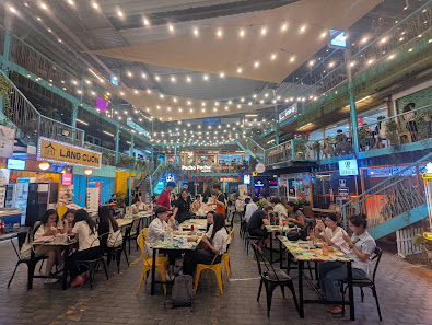 A bustling indoor dining venue in Thao Dien, Saigon, featuring multiple levels with string lights, numerous tables occupied by diners, visible signage