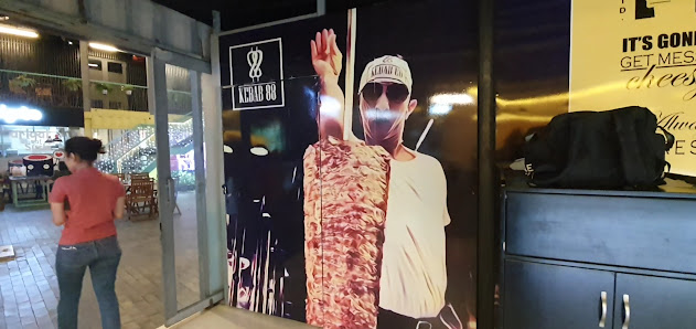 The image shows an interior view of a restaurant or food establishment named 'Kebab BBQ'. There is a large advertisement on the wall featuring a perso