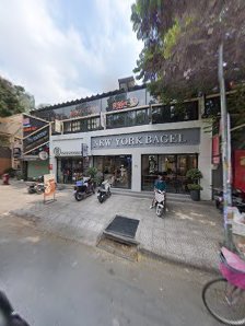 The image shows an exterior view of a storefront named 'New York Bagel' with motorcycles parked in front and trees visible on the left side.