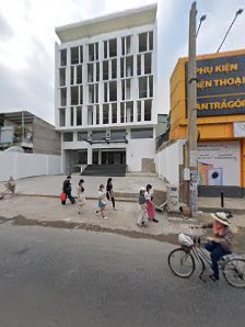 The image shows a street scene in Thao Dien, Saigon with several people walking and one person riding a bicycle past modern buildings.