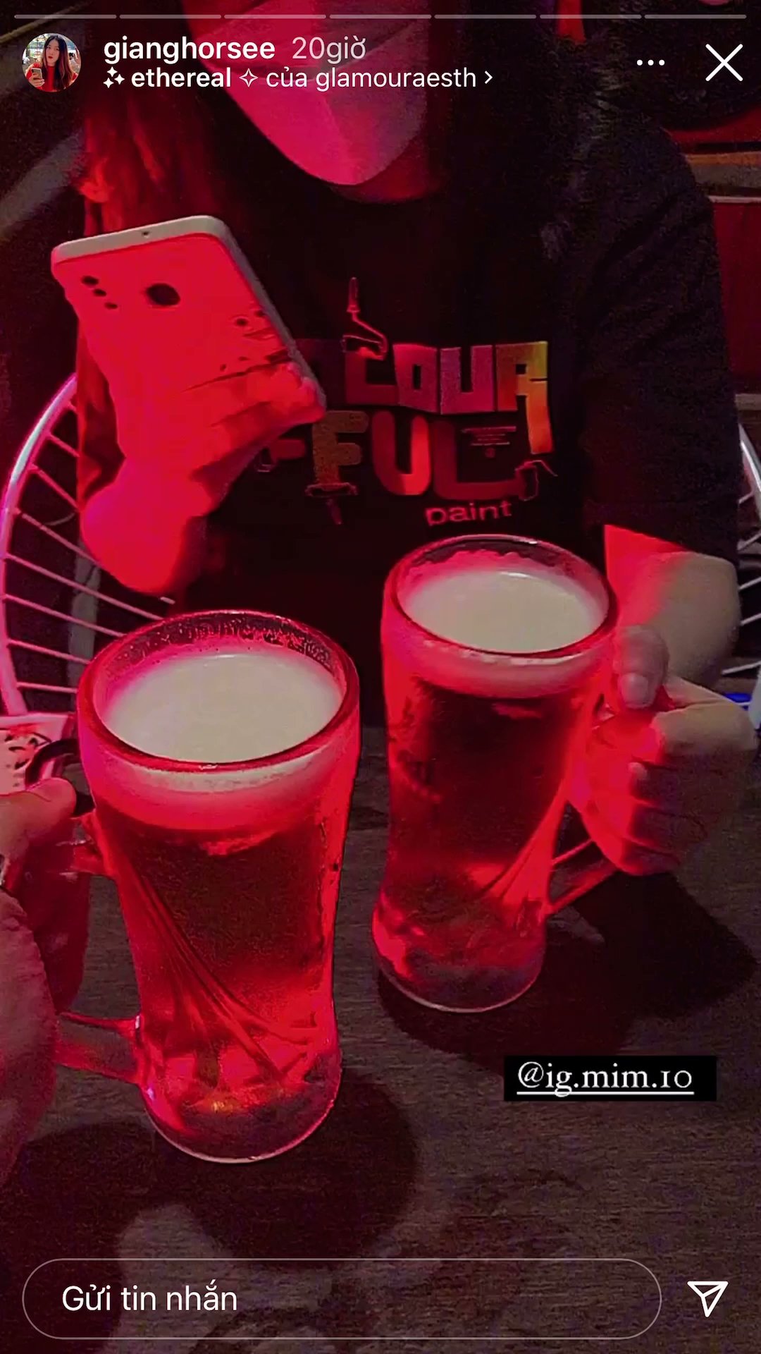 Two individuals are holding large mugs of beer in a dimly lit venue illuminated by red lighting.