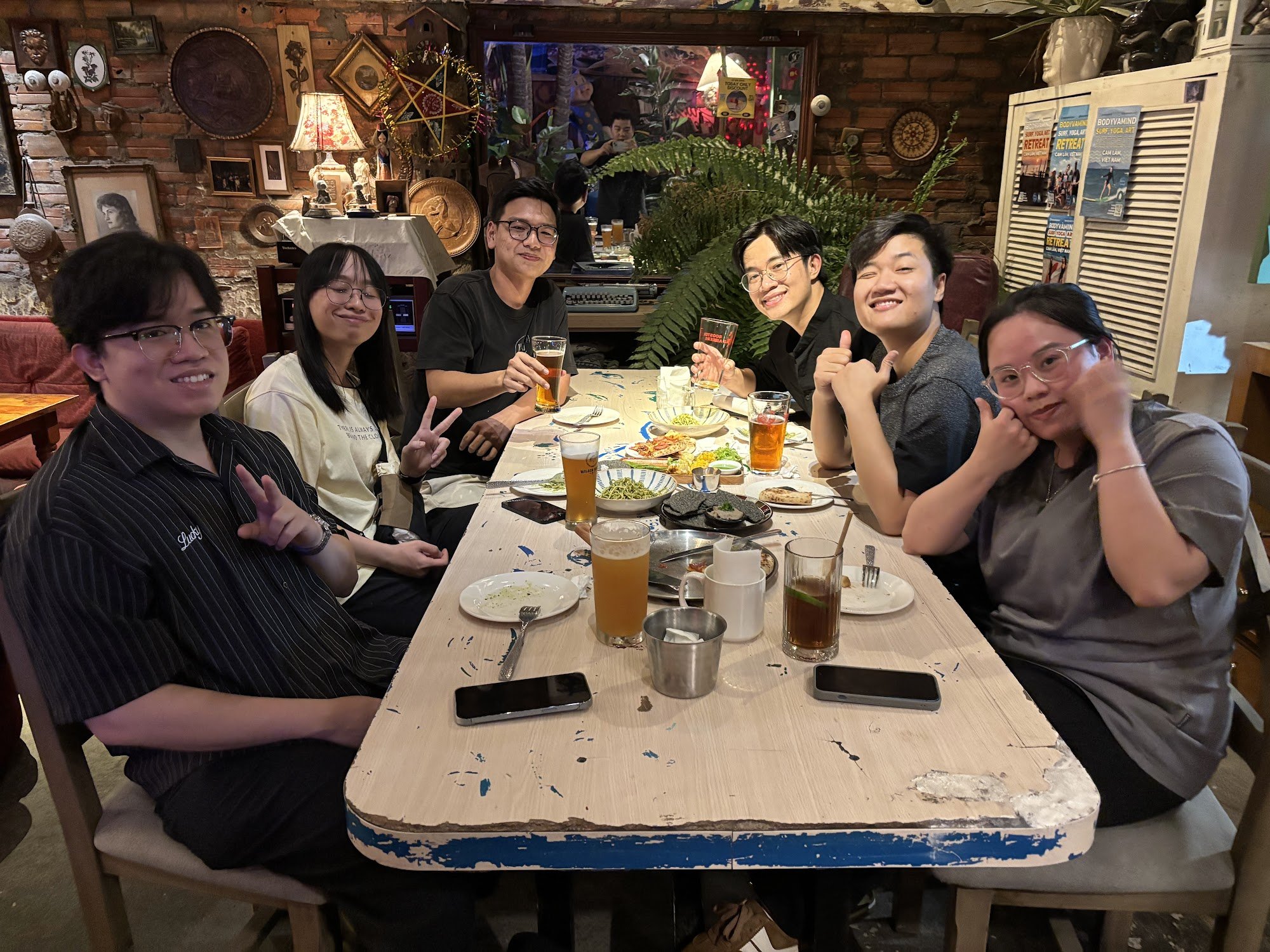 A group of people is seated around a table in what appears to be an indoor restaurant with rustic decor and various items on the wall, such as framed