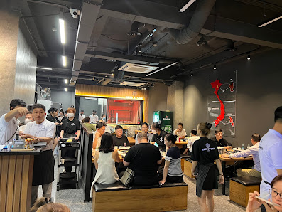 The image shows an interior view of a busy restaurant or food establishment in Thao Dien, Saigon. The space is modern with dark tones and industrial e