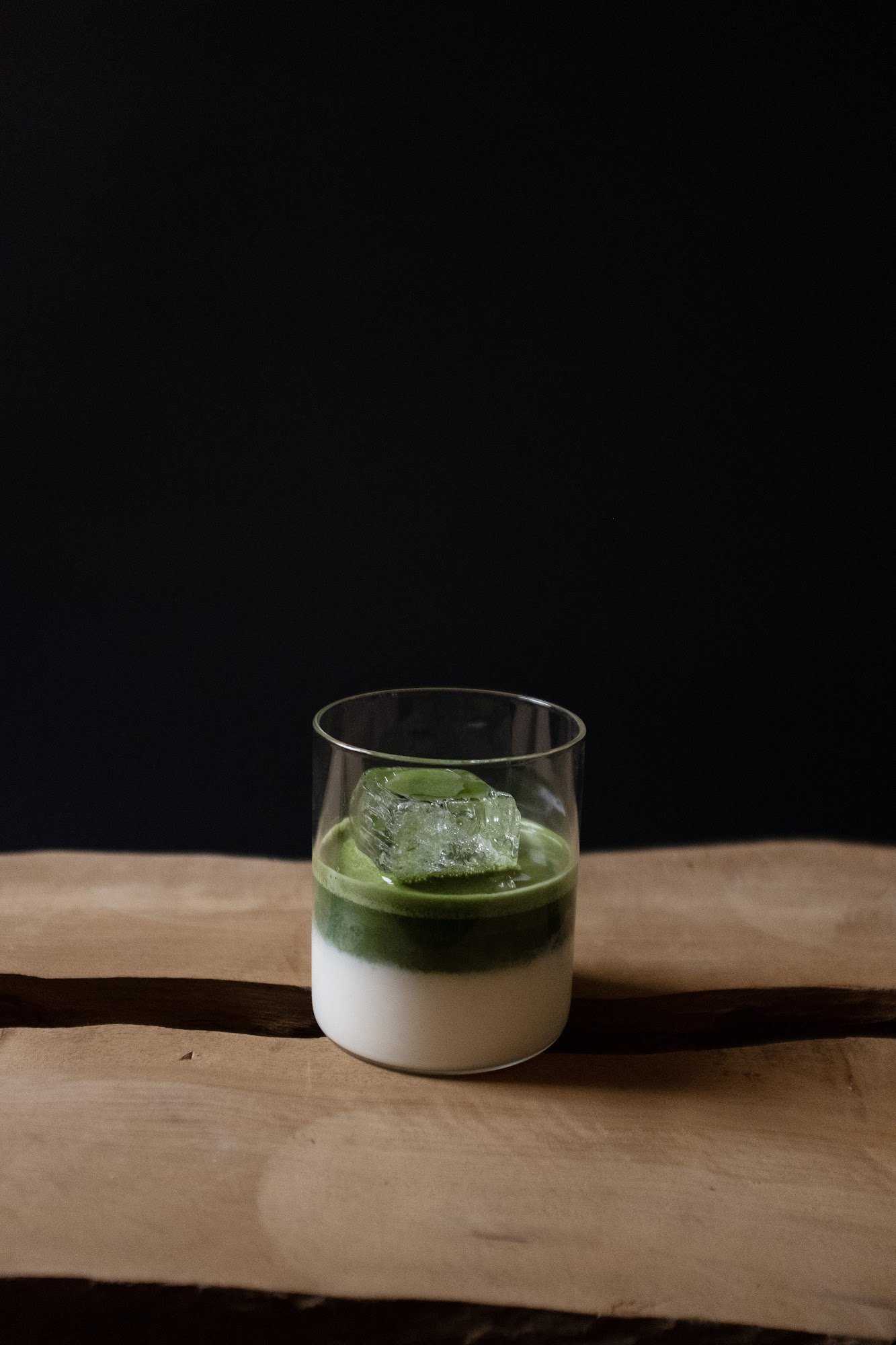 A layered drink in a glass on a wooden surface against a dark background.