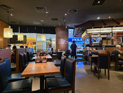 The image depicts the interior of a restaurant in Thao Dien, Saigon. It features multiple wooden tables with dark blue chairs, arranged in a spacious 