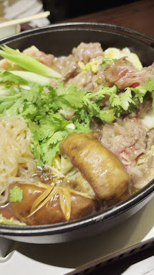 A bowl of hot pot containing various ingredients such as beef slices, mushrooms, enoki mushrooms, and garnished with green onions.