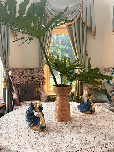 The image depicts an elegant interior setting featuring a round table adorned with decorative items such as blue and gold swan figurines, a vase of gr