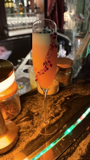 A close-up shot of a cocktail glass on a bar counter at Thao Dien, Saigon. The drink is garnished with what appears to be edible flowers and has a gra