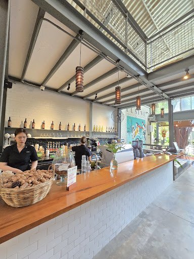 The image depicts the interior of a modern café or bar in Thao Dien, Saigon. It features a long wooden counter with a wicker basket of bread, various 
