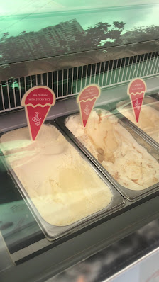 The image shows a display case in an establishment featuring three containers of ice cream or frozen dessert with red and white cone-shaped labels ind
