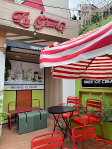 The image shows an exterior view of a colorful ice cream shop named 'Ice Cream'. The establishment has red and white striped awnings, bright orange ch