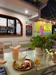 The image shows an outdoor dining area of a restaurant at night. The setting includes tables with food and drinks on them, as well as potted plants fo