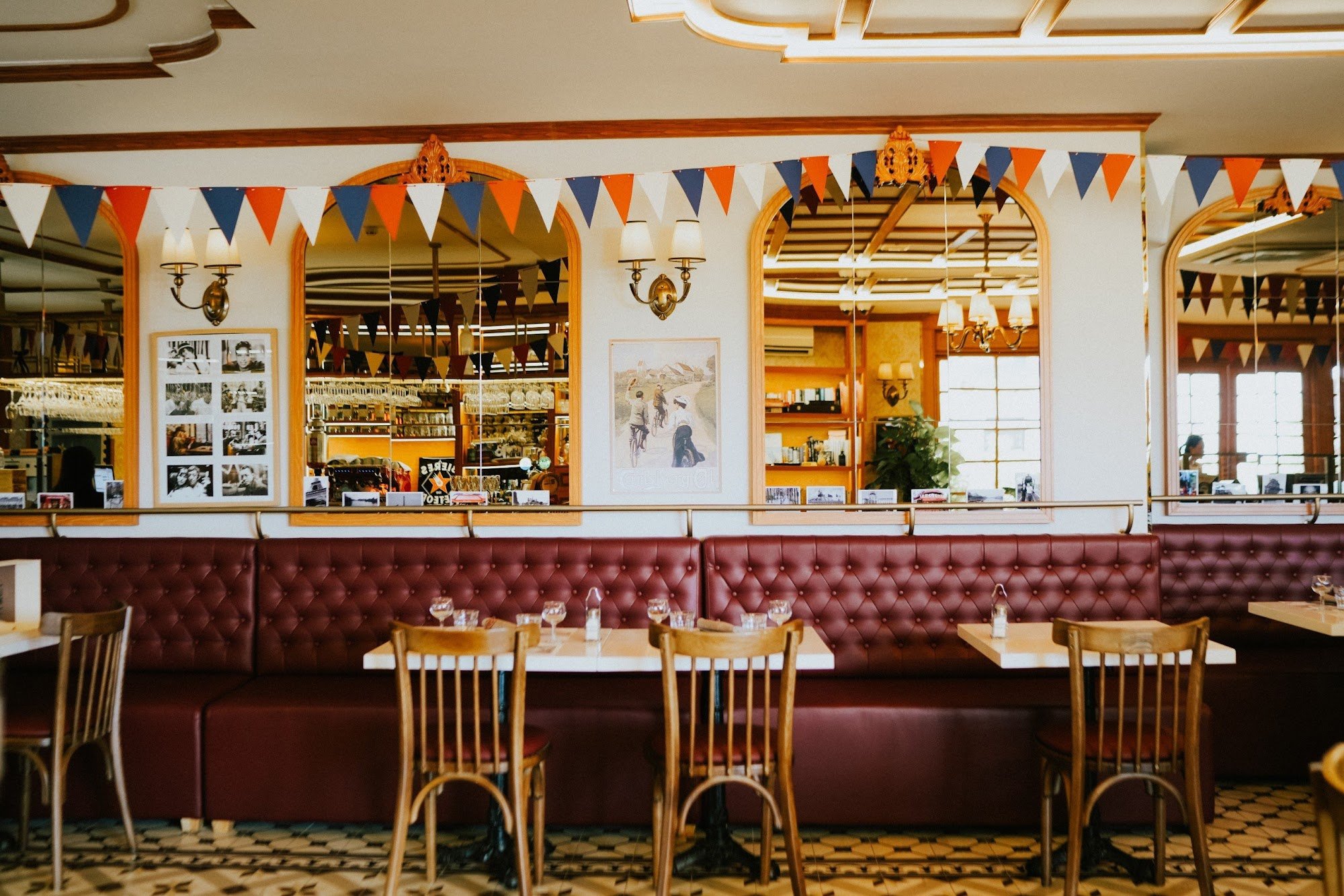 The image shows an interior view of a restaurant or cafe featuring red leather booth seating and wooden chairs at tables with white tablecloths, set a
