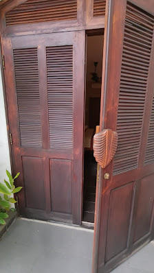 The image shows a close-up view of an open wooden door leading into what appears to be a traditional-style room with dark wood accents and bamboo blin