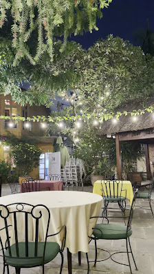 Outdoor dining area at night in Thao Dien, Saigon. Features round tables with white tablecloths, green chairs, string lights hanging between trees, an