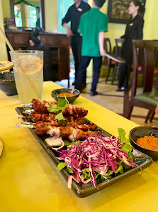 A vibrant interior shot of a restaurant in Thao Dien, Saigon. A yellow table holds a platter with fried items (likely spring rolls or similar), purple