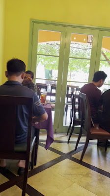 Indoor dining area with yellow walls, glass doors leading to an outdoor space with greenery visible through the doors. Several people are seated at ta