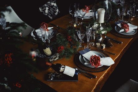 The image depicts a beautifully set dining table adorned with festive decorations such as red berries and pine branches in glass vases, wine glasses f
