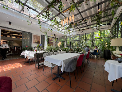 The image depicts an elegant indoor dining area with terracotta flooring, white tablecloths, and a mix of chairs (some with red cushions). There are t