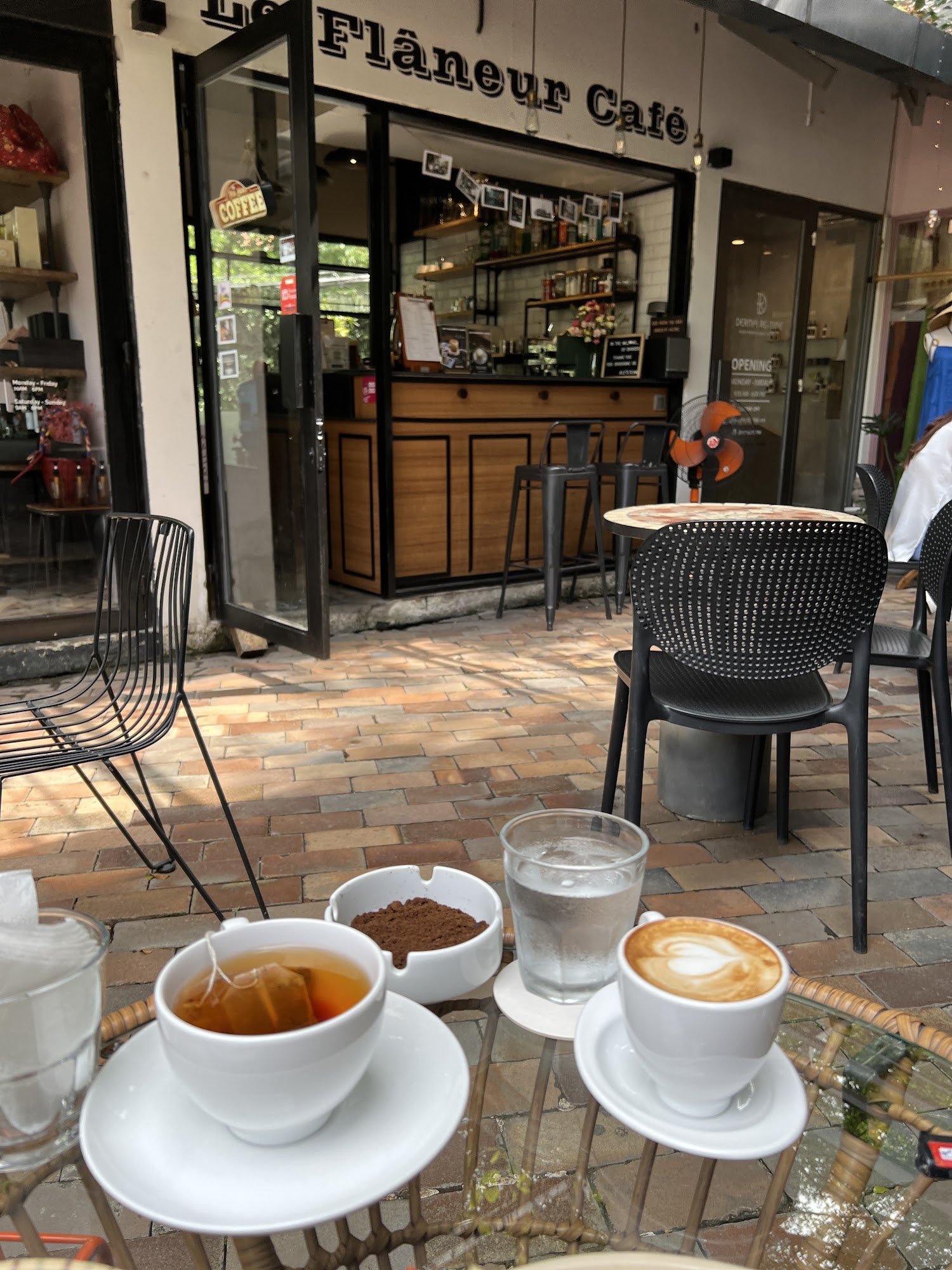 The image shows an outdoor seating area of a café named 'Flaneur Café'. There are several tables and chairs, with one table in the foreground containi