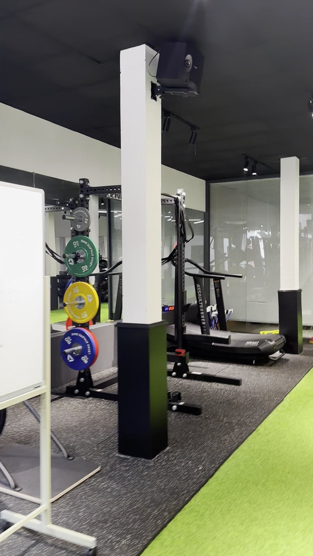 The image shows a modern gym interior equipped with various exercise machines and weights on racks.