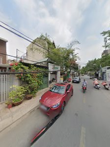 A street scene in Thao Dien, Saigon, featuring a red car parked along the curb, motorbikes traveling on the road, residential buildings with balconies