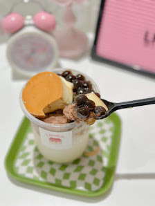 A close-up of a dessert cup containing yogurt or cream topped with various fruits and nuts.