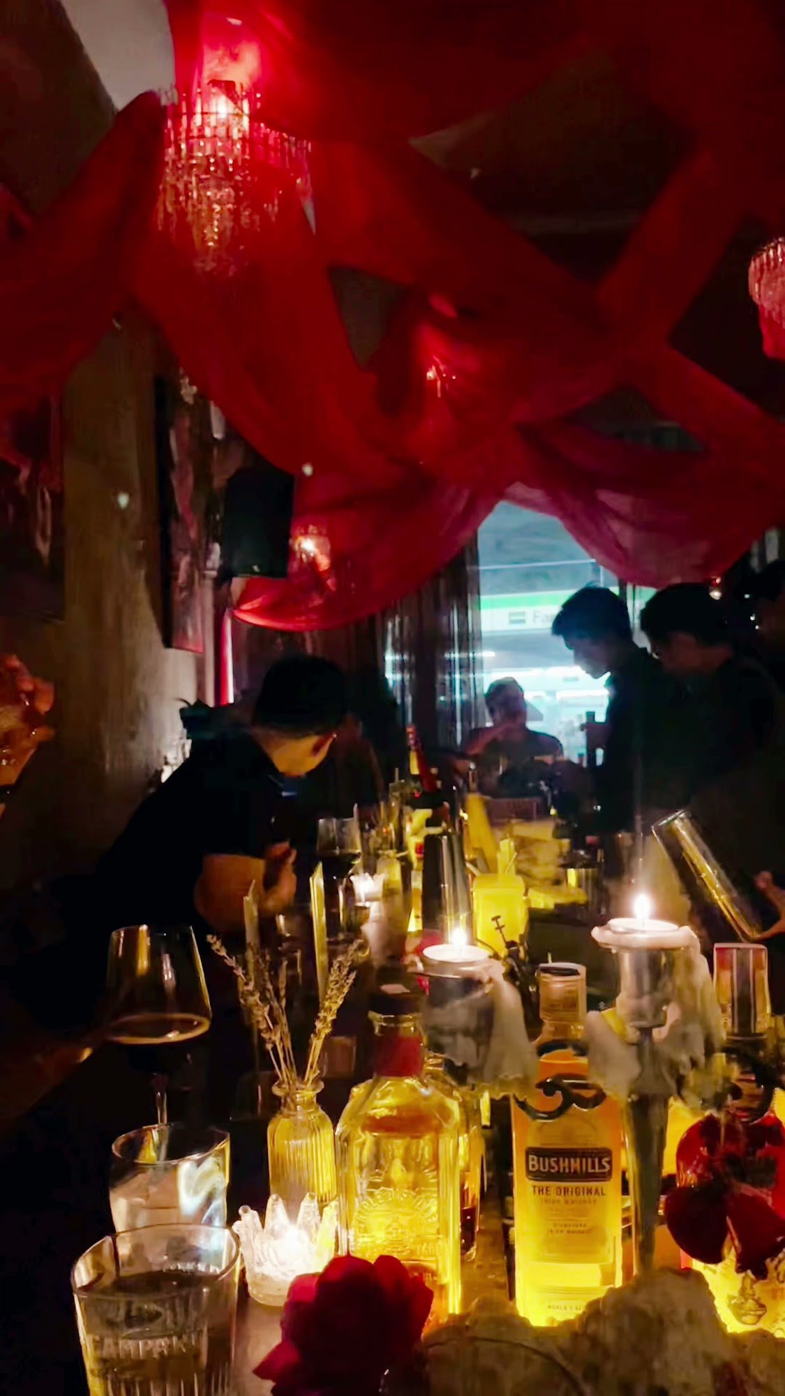 The image depicts an interior scene of a dimly lit bar or restaurant adorned with red decorative elements and hanging chandeliers, creating a cozy yet