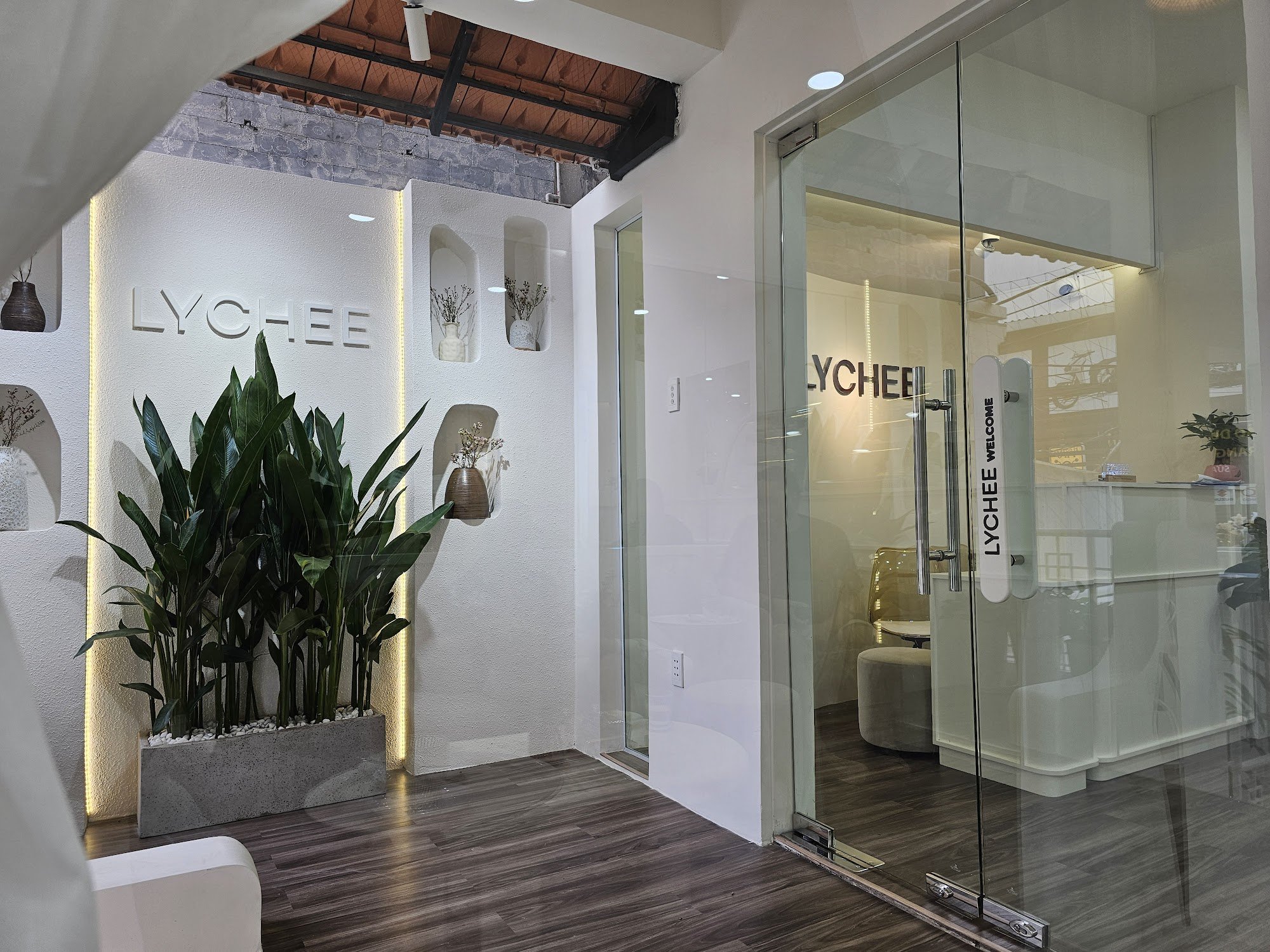 The image shows an interior view of a modern café named 'LYCHEE'. The space features clean lines with white walls and wooden flooring, complemented by