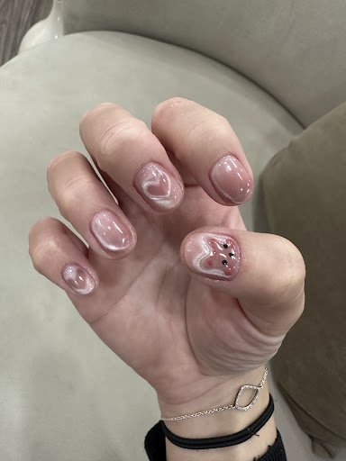 A close-up of a person's hand displaying intricately designed nail art featuring heart and star shapes with glittery pink polish on the nails, against